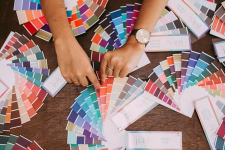 Mulher escolhendo uma cor em uma mesa com diversas cartelas de cores espalhadas.