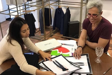 Uma mulher e um homem sentados em uma mesa analisando os croquis de seus uniformes.