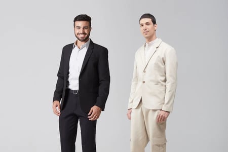 Dois homens vestindo diferentes modelos de terno, um na cor preta e o outro bege