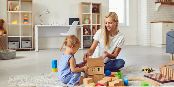 Babá brincando de construção com uma criança sentada no tapete.