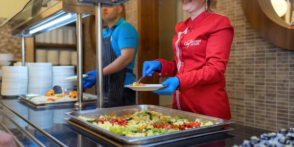 Colaboradores de um restaurante, vestidos com uniforme, servindo refeições