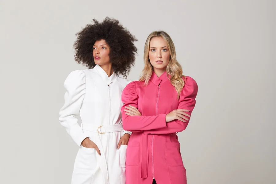 Duas mulheres vestidas com jaleco de esteticista, um na cor branca e outro na cor rosa