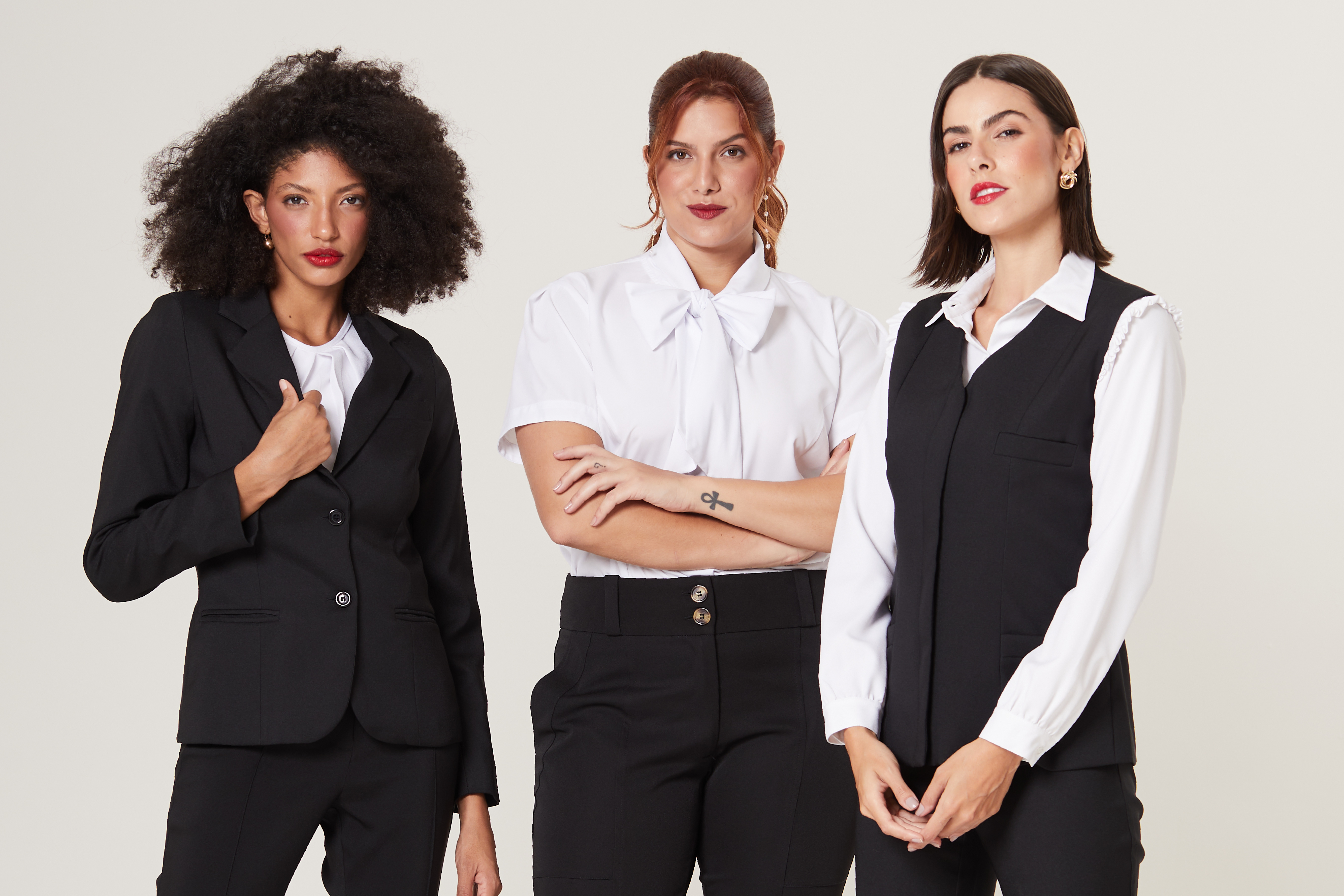 3 modelos em pé vestidas com uniformes preto e branco de alfaitaria