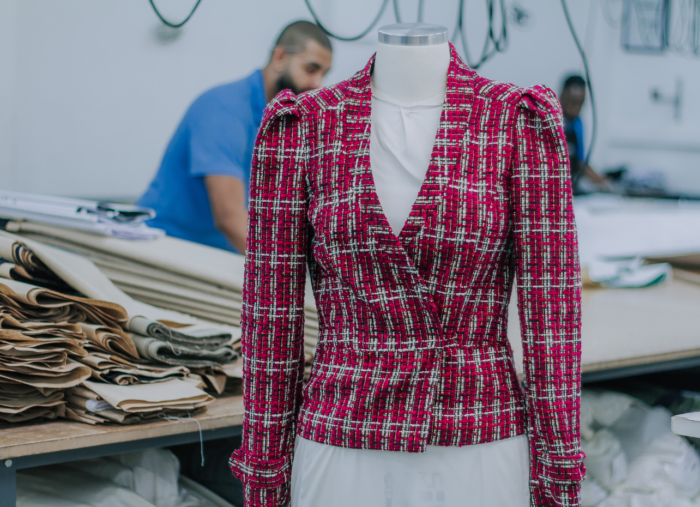 manequim só de busto vestido com um blazer de tweet rosa. Ao fundo uma fábrica de confecção de uniformes.